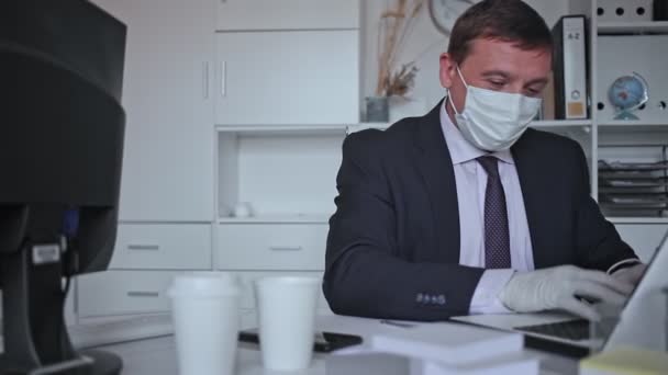 Homme concentré dans un équipement de protection individuelle jetable travaillant dans un bureau d'affaires à l'aide d'un ordinateur portable, nouvelle normale en raison de l'épidémie de coronavirus — Video