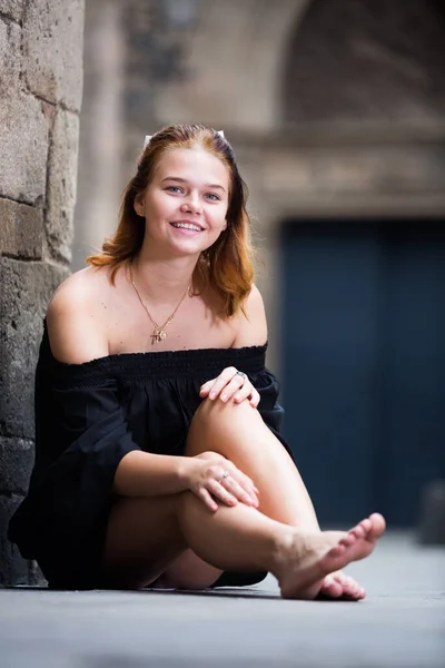 Joven hembra sentada descalza cerca de la pared de piedra — Foto de Stock