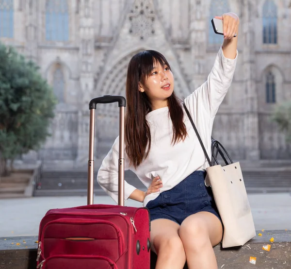 Aantrekkelijke jonge Chinese vrouw zit op stenen trap en maakt selfies tegen de achtergrond van bezienswaardigheden — Stockfoto