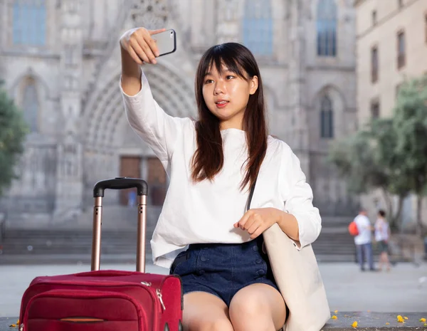 Mulher chinesa jovem atraente senta-se na escada de pedra e faz selfies contra o fundo das vistas — Fotografia de Stock