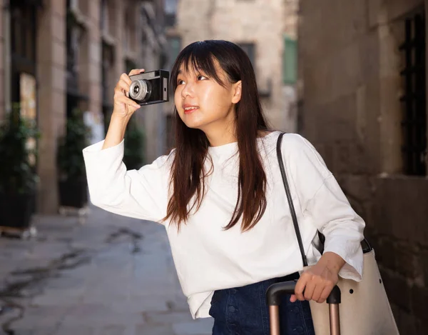Молодая китаянка-путешественница прогуливается с багажом по городу, фотографируя достопримечательности — стоковое фото