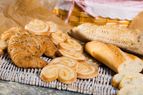 Wheat and grain baguettes, croissants and biscuits on wicker mat — Stock Photo, Image