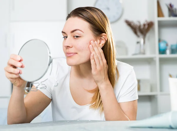 Cheerful woman is concentrared looking on her face in the mirror — Stock Photo, Image