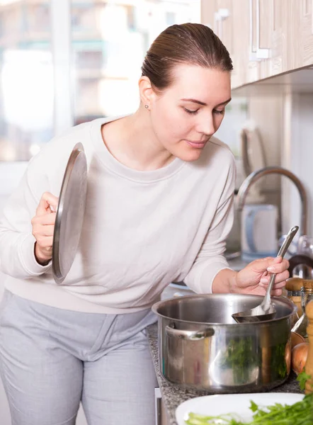 Ung kvinna lagar soppa och saltar den i köket — Stockfoto