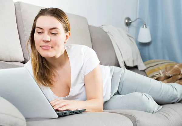 Porträtt av glad kvinna som arbetar med laptop på soffan — Stockfoto