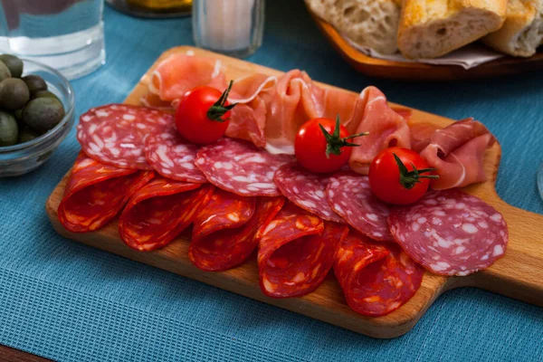 Spanish tasty meal slicing sausages and ham with tomatoes at wooden desk — Stock Photo, Image