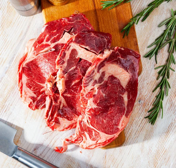 Unfinished beef steak with sprig of rosemary on cutting board — Stock Photo, Image