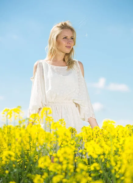 Ung kvinna i gul oljeväxter rapsfält poserar i vit klänning — Stockfoto