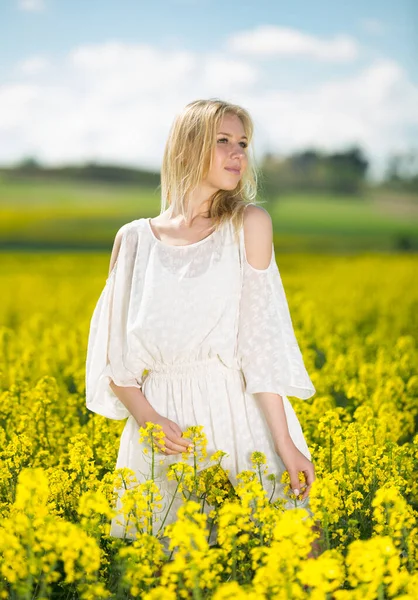 Lány pózol nemi erőszak mag virágok mező pózol fehér ruhában a napsütéses napon — Stock Fotó