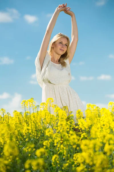 Gelukkig meisje stretch zichzelf in verkrachting zaad bloemen veld poseren in wit jurk — Stockfoto