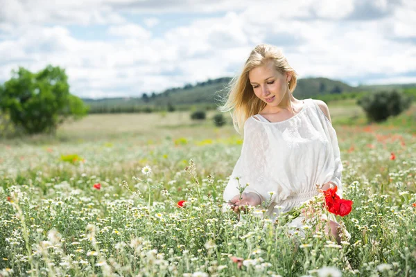 Frau im weißen Kleid posiert auf Feldern mit Gänseblümchen und hält Mohn in der Hand — Stockfoto