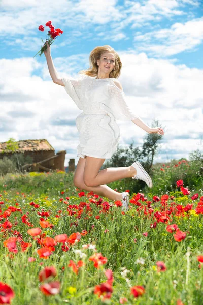 Jovem fêmea em vestido branco pulando no campo de papoula de flores selvagens — Fotografia de Stock