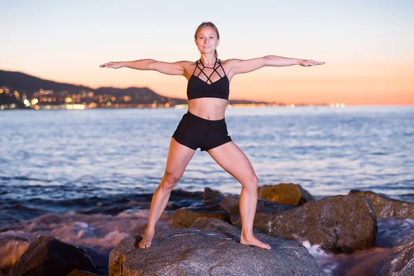 Mujer joven está practicando estiramiento cerca del mar — Foto de Stock