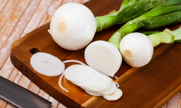 Tagliare i bulbi di cipolla giovane verde sulla scrivania di legno durante la cottura — Foto Stock