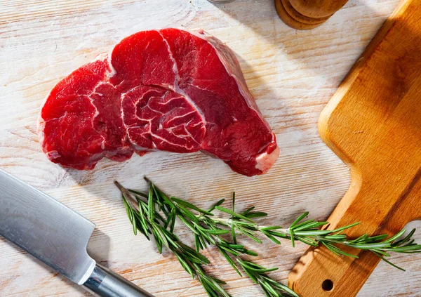 Unfertiges Rindersteak mit Rosmarinzweig auf Schneidebrett — Stockfoto