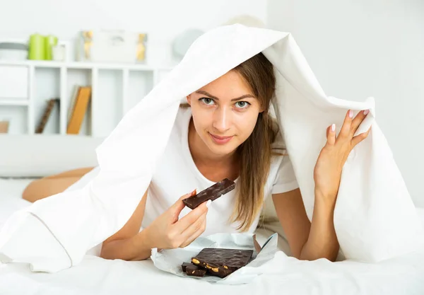 Donna mangiare cioccolato a letto — Foto Stock