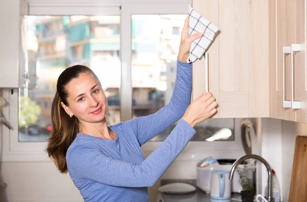 Uśmiechnięta kobieta sprząta powierzchnię w kuchni w domu — Zdjęcie stockowe