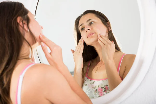 Молодая женщина трогает лицо и использует зеркало в спальне — стоковое фото
