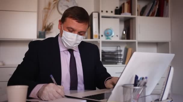 Zakenman in beschermend masker werkt alleen met laptop en papieren op kantoor — Stockvideo