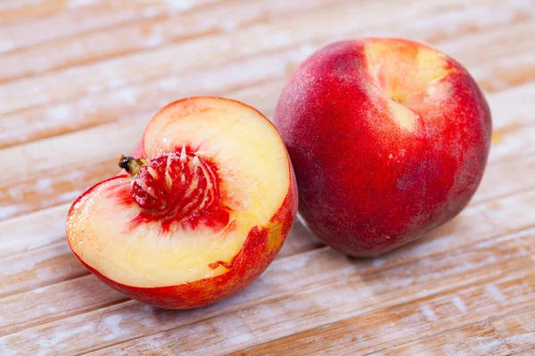 Hele en halve verse rode perziken op houten tafel. — Stockfoto