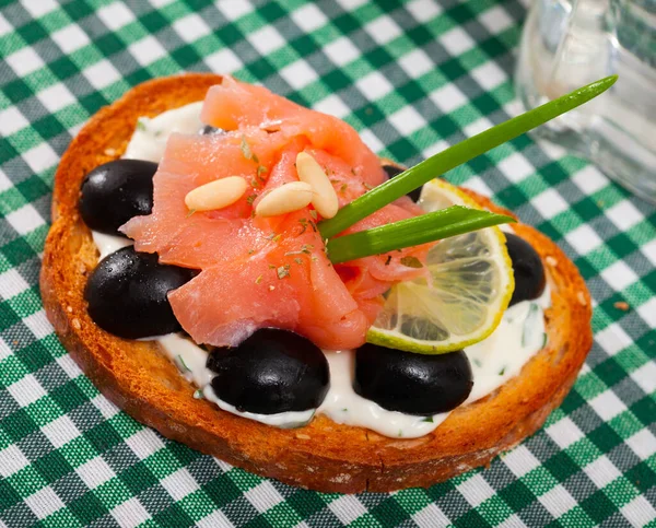 Toast mit Lachs, Oliven und cremiger Soße auf kariertem Textil — Stockfoto