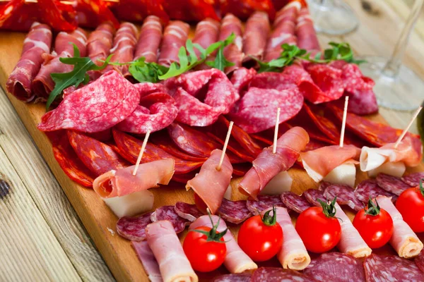 Fatiando salsichas fuet, presunto, salame, chouriço com tomate cereja e azeitonas — Fotografia de Stock