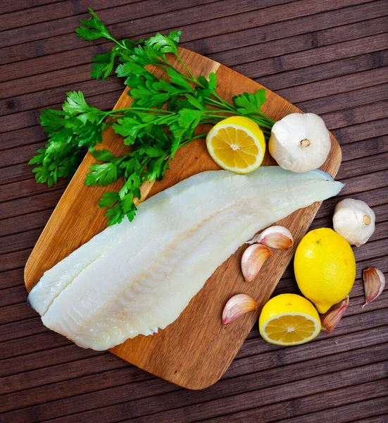 Raw cod fillet with garlic and lemon on wooden surface — Stock Photo, Image