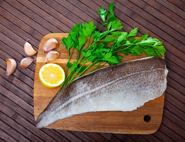 Filete de bacalao crudo sobre una superficie de madera con ajo y verduras — Foto de Stock