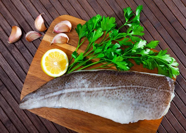 Filete de bacalao crudo sobre una superficie de madera con ajo y verduras — Foto de Stock