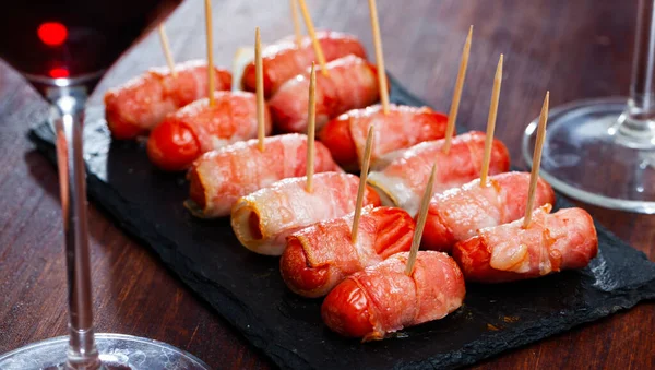 Rolled bacon with sausages on black dish — Stock Photo, Image