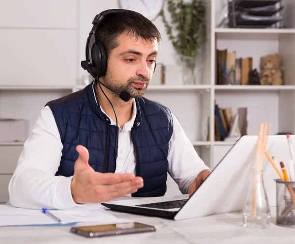 Mladý muž zaměstnanec se sluchátky a notebookem u stolu — Stock fotografie