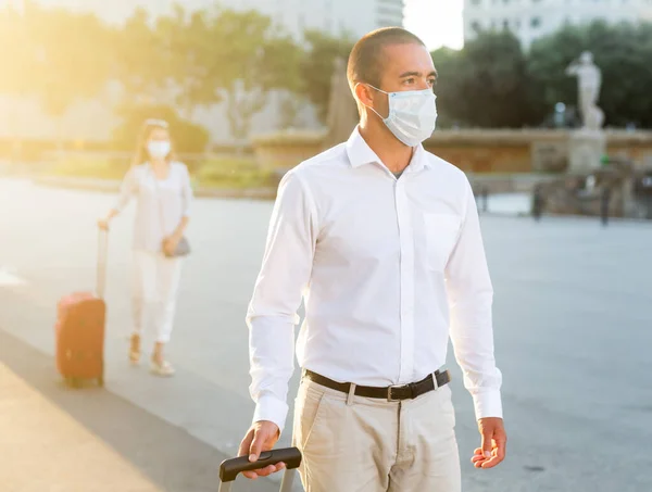 Viajante em máscara médica passeando com bagagem ao longo da rua da cidade — Fotografia de Stock