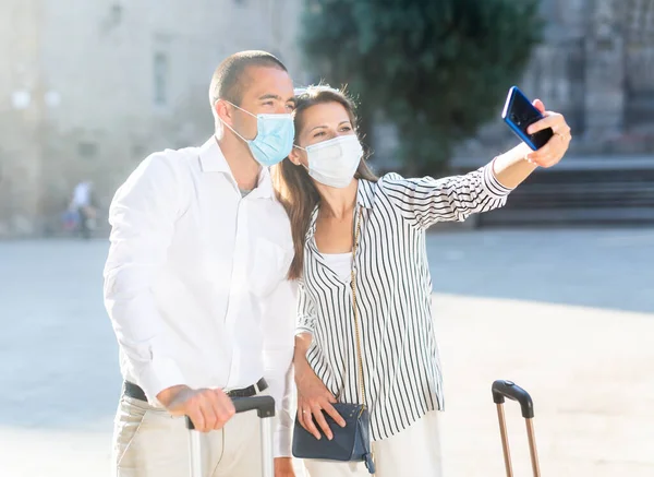 Casal de viajantes em máscaras médicas fazendo selfie com telefone — Fotografia de Stock