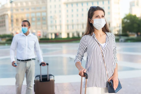 도시를 따라 짐을 싣고 질주하는 의료용 마스크를 쓴 여자 여행자 — 스톡 사진