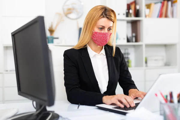 Donna d'affari in maschera medica colorata che lavora con il computer portatile — Foto Stock