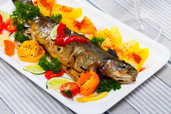 Tasty baked whole trout with vegetables, greens and lemon served — Stock Photo, Image