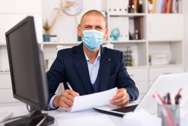 L'impiegato in una maschera protettiva lavora dietro computer portatile — Foto Stock