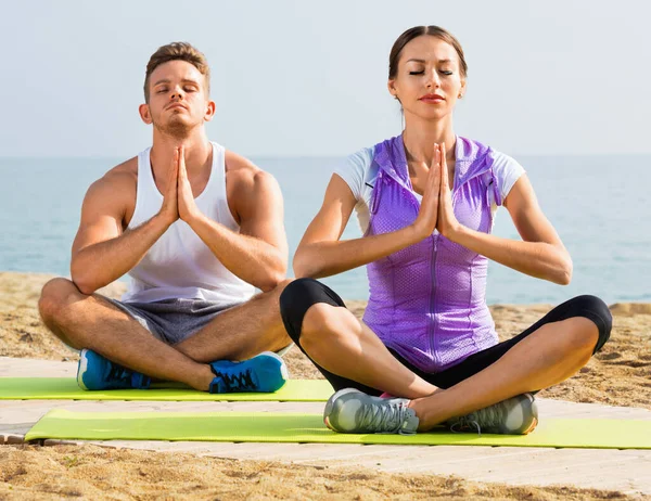 Donna e uomo seduti a gambe incrociate fanno yoga pose sulla spiaggia — Foto Stock