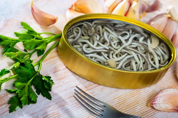 Lata aberta de enguias em conserva e alho com verduras à mesa — Fotografia de Stock