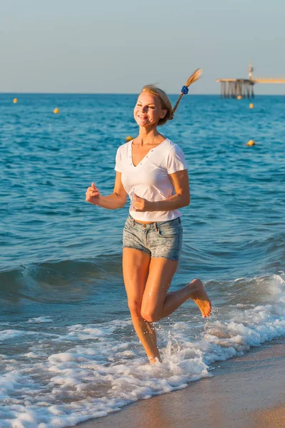 Sorrindo mulher adulta em camiseta branca está correndo na praia — Fotografia de Stock