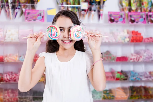 Feliz niña pequeña con piruleta en palo en la tienda de dulces —  Fotos de Stock