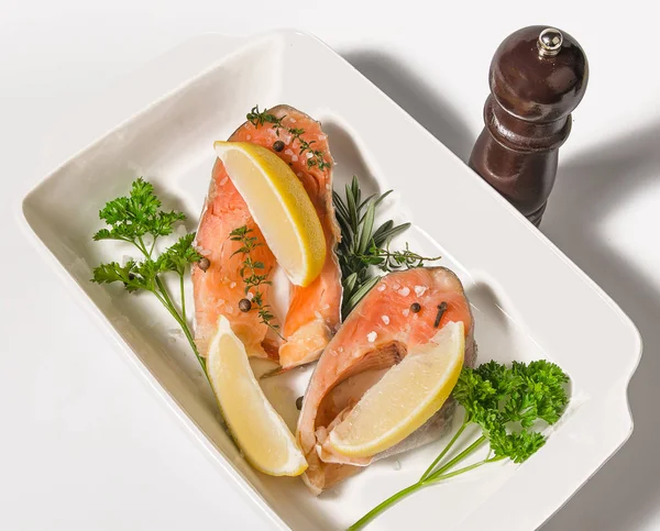 Two steaks trout fillet with spices and lemon in baking dish on white background