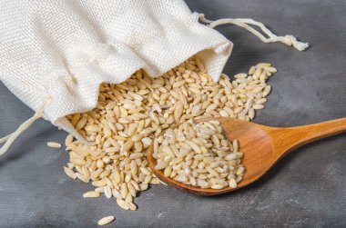 pearl barley in burlap bag and spoon on dark background