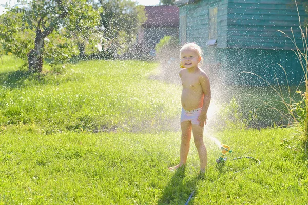 Lapsi leikkii puutarha sprinkleri puiden alla kuvapankkikuva