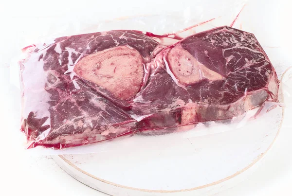 Vacuum sealed fresh beef meat on white wooden background. Top view