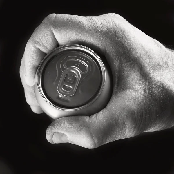 Beer can in hand on black background. Black and white