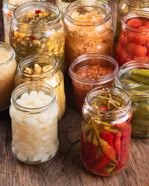 Different Fermented preserved vegetables in glass jars on a rustic wooden background