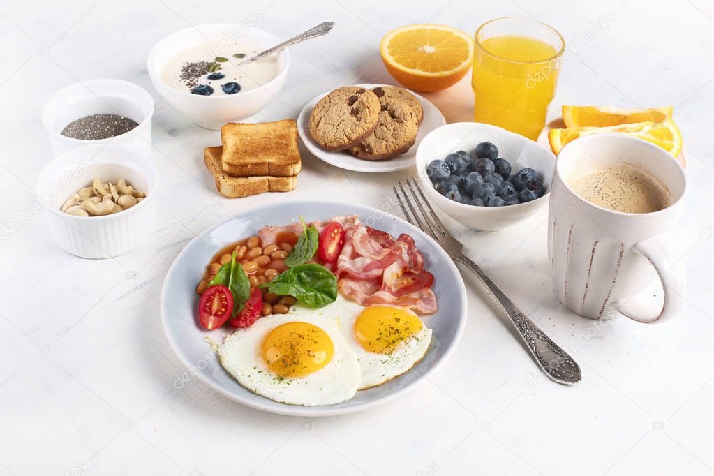 Breakfast with fried eggs, bacon, orange juice, yogurt and toasts.