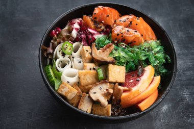 Somon, quinoa, sebze, meyve ve tofu koyu arka plan üzerinde kase poke