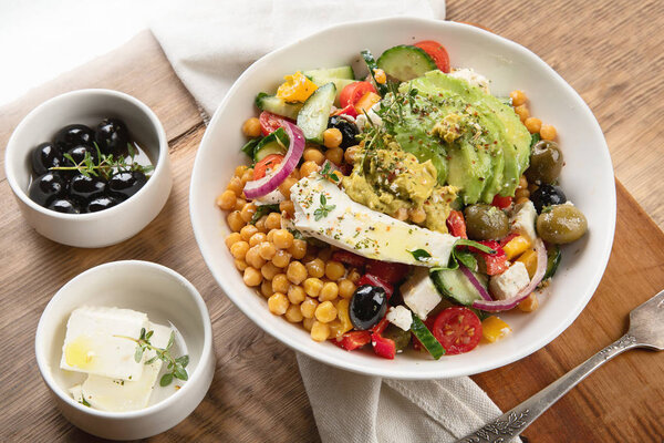 Чаша свежего салата с горохом, фета, оливки и авокадо на деревянном фоне
.
